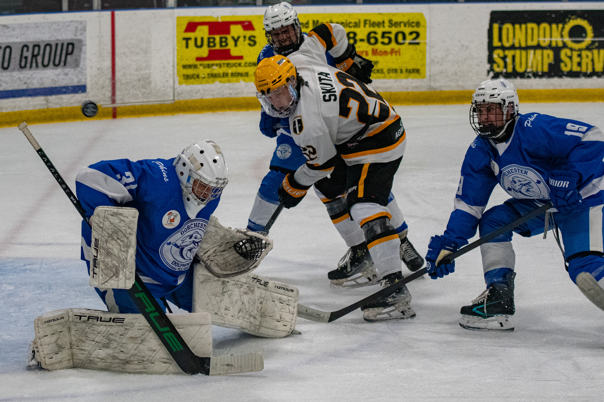 Dorchester Dolphins Charlie Keyes (19) and Tavistock Braves Jacob Skuta watch the puck deflect over goalie Brandon Mancari and the net.